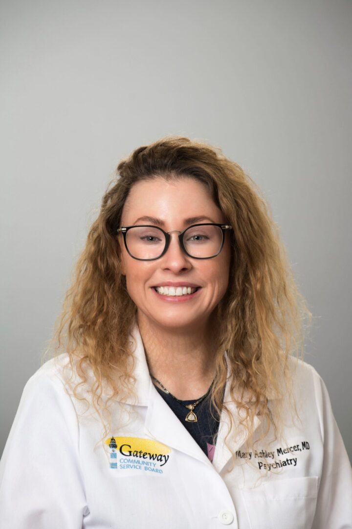 Person in white coat, smiling, wearing glasses.